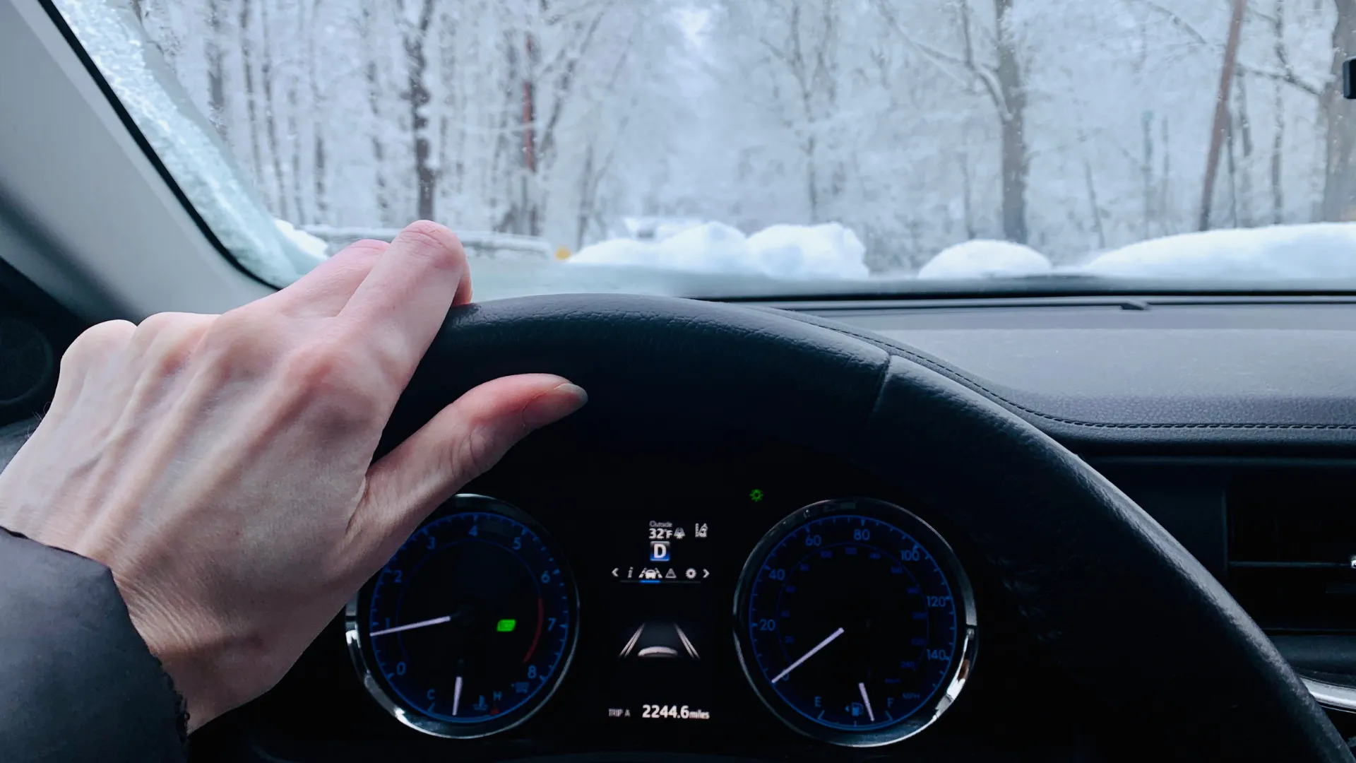 Winter Car Care Tips - Woman's hand gripping steering wheel of car with a snowy scene in the background